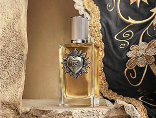 Dolce & Gabbana Devotion Parfumflakon mit silberner Kappe und herzförmigem Emblem steht in einer rustikalen Steinvertiefung. Im Hintergrund ist ein schwarzes Kissen mit goldenen Stickereien zu sehen.