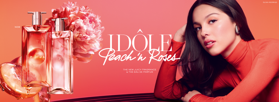 Werbebanner für Lancôme Idôle Peach in Roses Eau de Parfum mit zwei rosafarbenen Flakons, Pfingstrose und Pfirsich vor korallfarbenem Hintergrund sowie Model in passendem Outfit