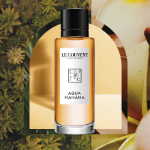 Parfümflakon der Marke Le Couvent mit schwarzem Deckel und weißem Etikett, Duftname ‚Aqua Mahana‘. Der Flakon steht vor einem tropischen Hintergrund mit Blüten und Pflanzen in Gelb- und Grüntönen, eingerahmt von einem stilisierten Bogen.