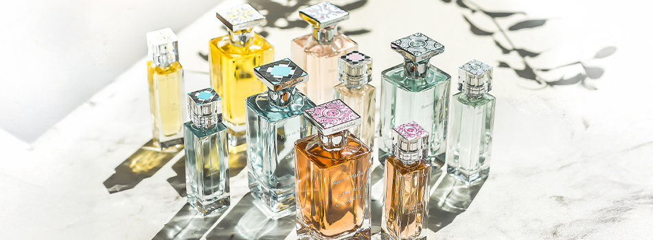 Mehrere luxuriöse Parfumflaschen von Rose et Marius auf einer Marmoroberfläche mit Licht- und Schattenspiel.