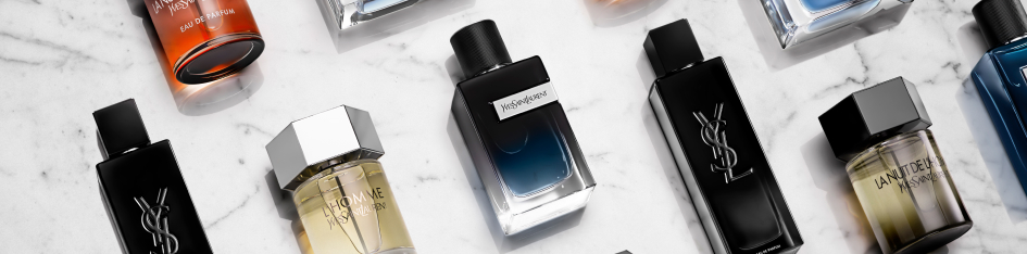 Kategoriebanner Herrendüfte von Yves Saint Laurent: Mehrere YSL-Parfumflakons für Herren, darunter Y und L’Homme, liegen verteilt auf einer hellen Marmoroberfläche in Schwarz-, Blau- und Goldtönen.
